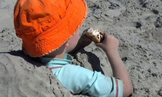 Junge sitzt eingebuddelt im Sand und isst