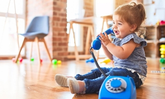 Kleinkind sitzt auf Boden und spricht begeistert in ein Spielzeugtelefon 
