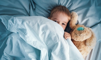 Kleinkind mit Teddy liegt im Bett und hat die Augen offen