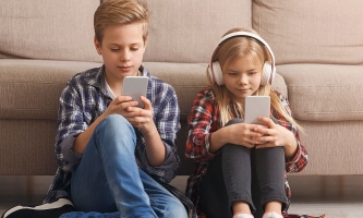 Kinder sitzen vor Sofa und schauen aufs Handy 