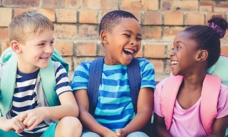 Drei Kinder sitzen nebeneinander und lachen 