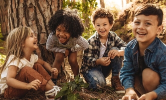 Kinder sitzen lachend auf Waldboden und spielen 