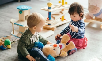 Zwei Kinder spielen mit Stofftier und sprechen mit ihm 