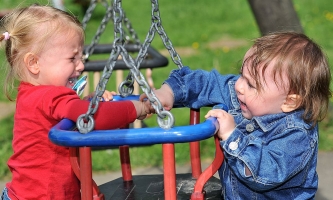 Zwei Kinder streiten auf Spielplatz um Schaukel und weinen 