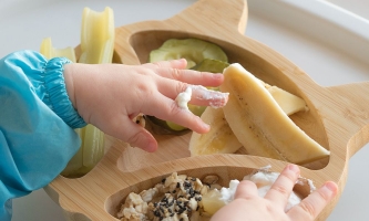 Hände von Kleinkind in Teller mit Essen 