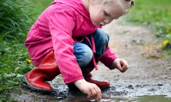 Mädchen in Regenkleidung spielt in Pfütze