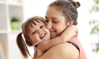 Mutter und kleine Tochter umarmen sich liebevoll und lächeln glücklich 