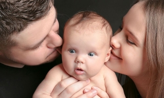 Vater und Mutter küssen Baby, Baby guckt erstaunt 