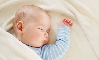 Säugling in hellblaumen Strampelanzug schläft ruhig in einem Bett