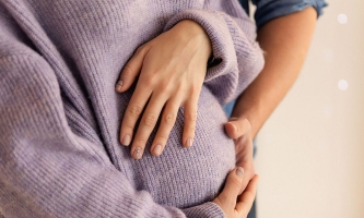 Werdende Eltern umfassen den Bauch der Schwangeren liebevoll mit den Händen 
