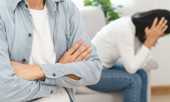 Paar sitzt schweigend und voneinander abgewandt nach Streit auf Couch im Wohnzimmer 