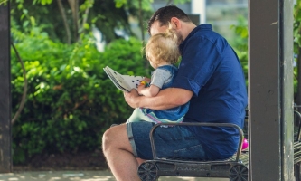 Vater sitzt mit Kind auf Bank und liest ihm vor 