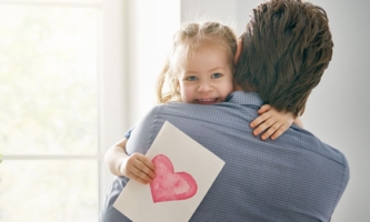 Tochter auf Arm von Vater hält Blatt mit rotem Herz in der Hand