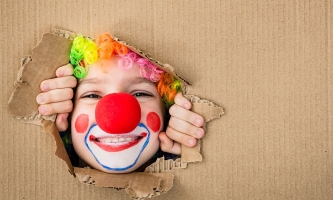 Als Clown verkleidetes Kind schaut durch ein Loch in einem Pappkarton
