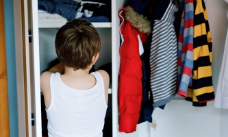 Kind steht vor Kleiderschrank und sucht Kleidung aus 