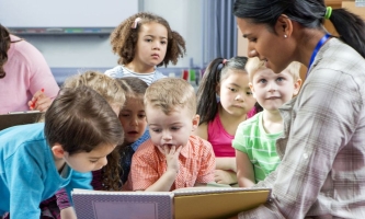 Kindergartenkinder lesen in Buch mit Erzieherin 