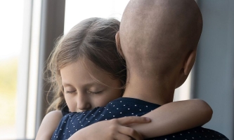 Mädchen umarmt innig seine Mutter, die Krebs hat und deren Kopf kahlgeschoren ist 