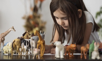 Mädchen spielt versunken mit Tierfiguren, die auf Tisch aufgereiht sind 