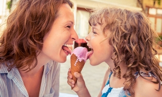 Mutter und Kind lecken lachend zusammen an einem Erdbeereis 