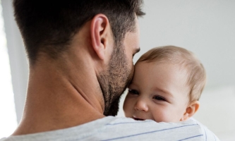 Vater hält Baby auf dem Arm, das zufrieden lächelnd über seine Schulter schaut 