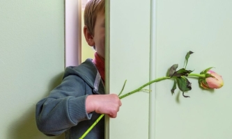 Kind mit Rose in der Hand spitzt durch halb geöffnete Zimmertür 