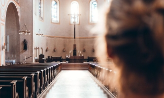 Frau schaut von hinten in leeren Kirchenraum