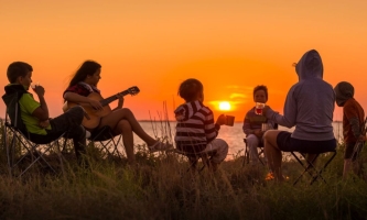 Kinder und Jugendliche im Kreis mit Gitarre im Sonnenuntergang