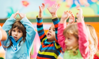 Drei Kinder halten ihre Arme nach oben und machen Bewegungen zu einem Lied nach.