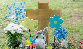 Kindergrab mit Kreuz, Kuscheltieren und bunten Windrädern 