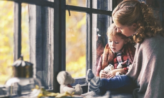 Eine Mutter sitzt mit ihrem Kind am Fenster, sie kuscheln sich aneinander.