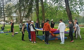 Kinder und Jugendliche spielen in Park mit buntem Tuch 