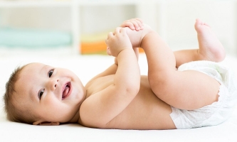 Baby liegt lachend im Bett und spielt mit seinen Füßchen 