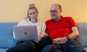 Tochter und Vater sitzen auf Sofa und schauen in Laptop 