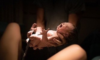 Geburt neugeborenes Baby mit Nabelschnur wird über Bauch von Mutter gehalten 