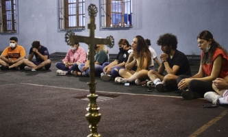Junge Männer und Frauen sitzen im Kreis um ein Kreuz und beten 