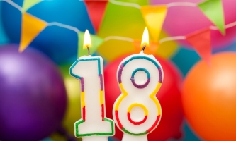 brennende Geburtstagskerzen als Zahl 18 mit bunten Luftballons im Hintergrund