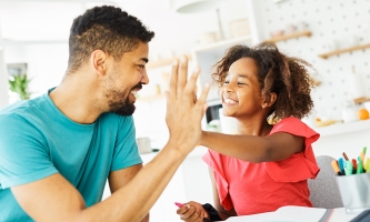 HIgh five zwischen einem Mädchen und ihrem Vater, beide lachen dabei.