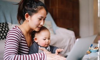 Mutter an Laptop zuhause mit Baby auf dem Schoß