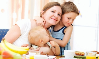 Mutter lachend mit zwei Kindern am Esstisch 