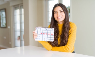 Ein Mädchen hält lächelnd einen Kalender in der Hand, in dem ihre Tage eingezeichnet sind.