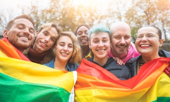 Queere Menschen halten eine Regenbogenfahne in der Hand und lächeln.