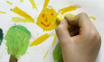 Kinderhand malt Sonne mit Wachsmalkreiden 