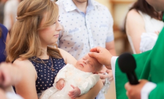 Priester salbt bei Taufe Kind mit Chrisamöl