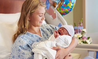 Teenagermutter mit neugeborenem Baby in Krankenhausbett mit Luftballons und Blumen 