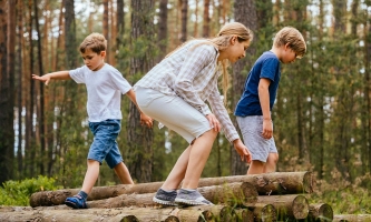 Kinder balancieren im Wald auf am Boden liegenden Holzstämmen 