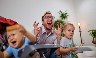 Zwei kleine Kinder essen, der Papa sitzt dazwischen, hebt seinen Kopf und schreit verzweifelt.