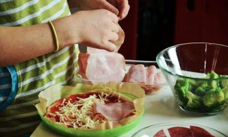 Kind belegt Pizza mit Käse, Schinken und Gemüse 