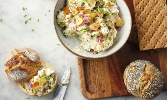 Kartoffelkäse in Schale mit Brot, Semmeln und Messer auf einem Brett 