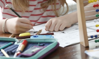 Hände von Kind beim Hausaufgabenmachen mit Heften und Federmäppchen 