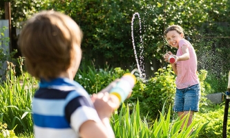 zwei Kinder spritzen sich im Garten mit Wasserspritzen nass